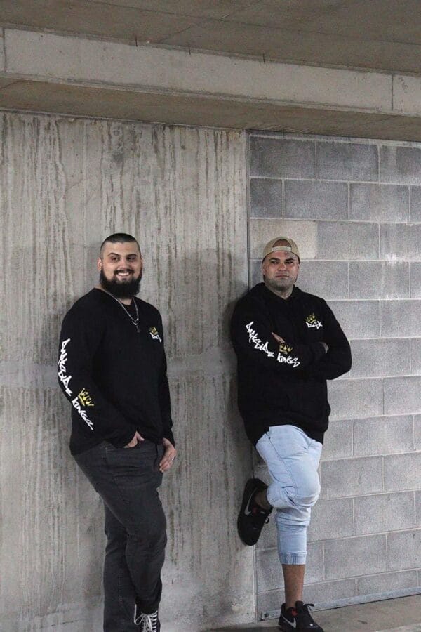 Male wearing a long sleeve DSK shirt standing next to a male wearing a DSK Hoodie