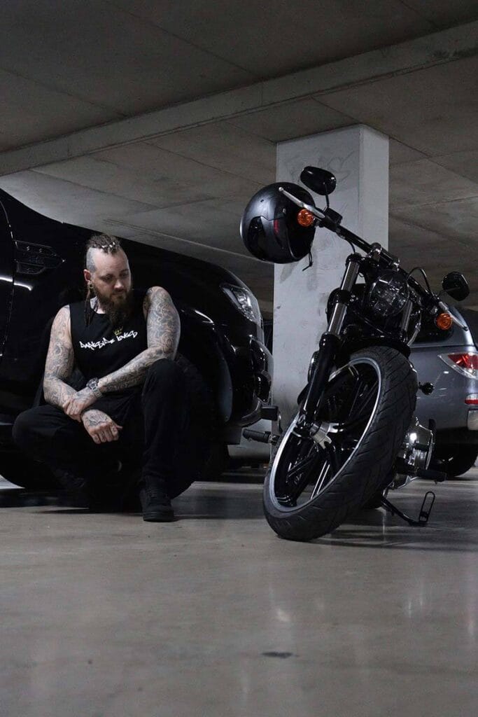 Front view of a male wearing a DSK Singlet crouching next to motorcycle