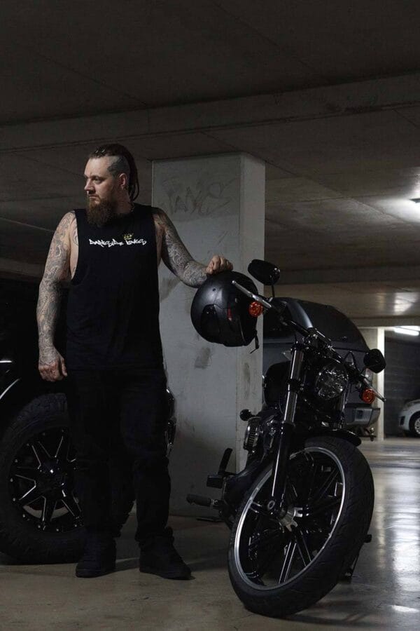 Front view of a male wearing a DSK Singlet standing next to motorcycle