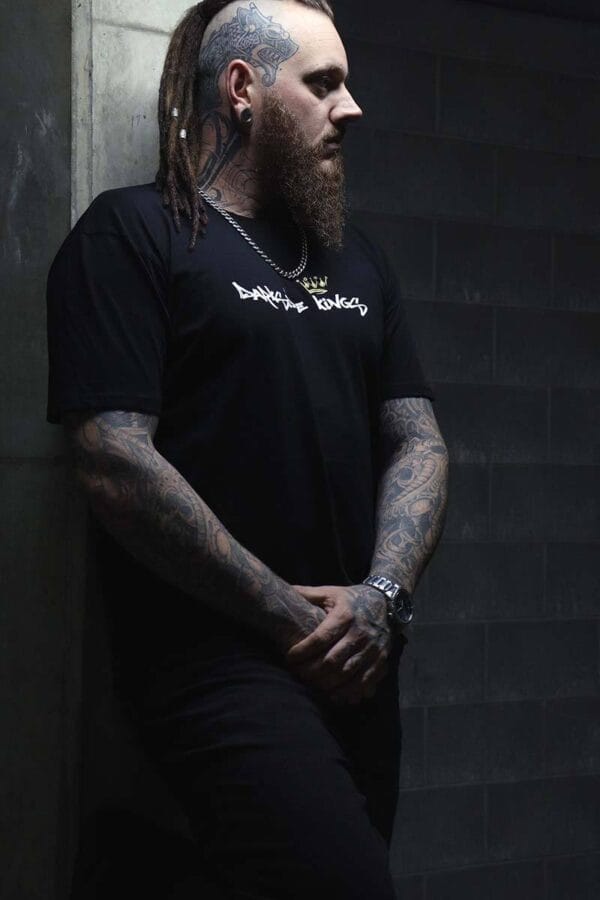 Male wearing a DSK T-shirt leaning against a concrete wall