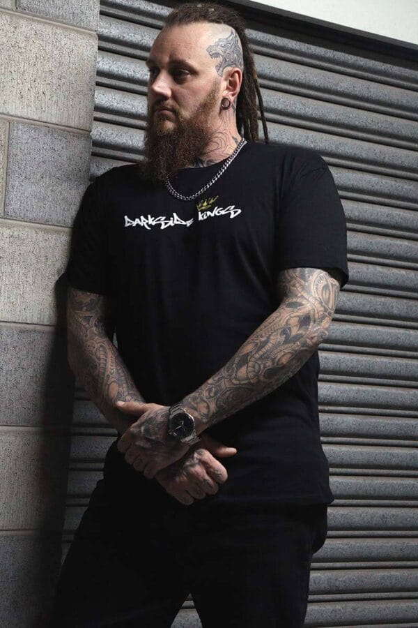 Male wearing a DSK T-shirt leaning against a concrete wall