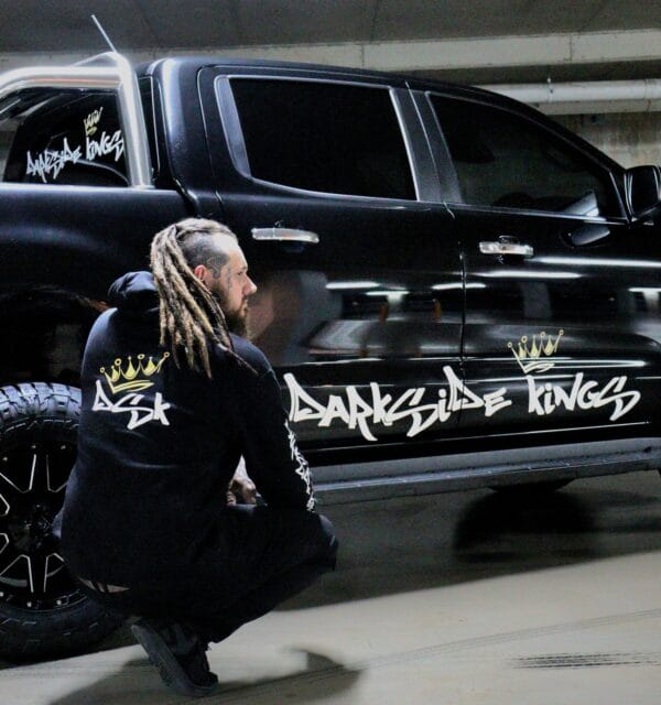Male wearing a DSK Hoodie crouching in front of a black Ford Ranger with a large DSK sticker across the doors