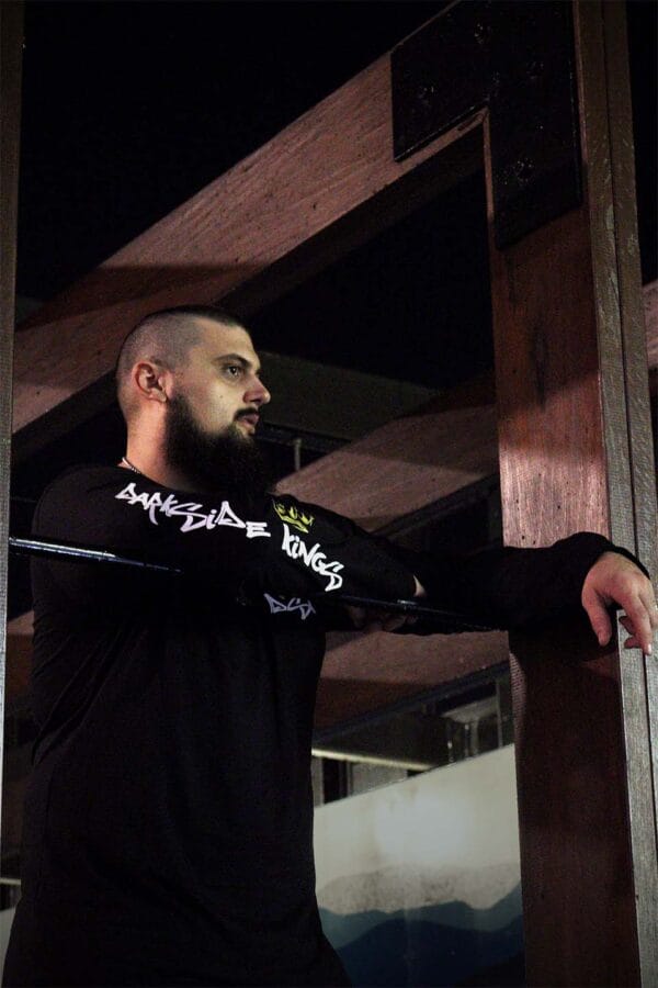 Male leaning over a rail wearing a black long sleeve shirt with a Darkside Kings logo printed down the sleeve
