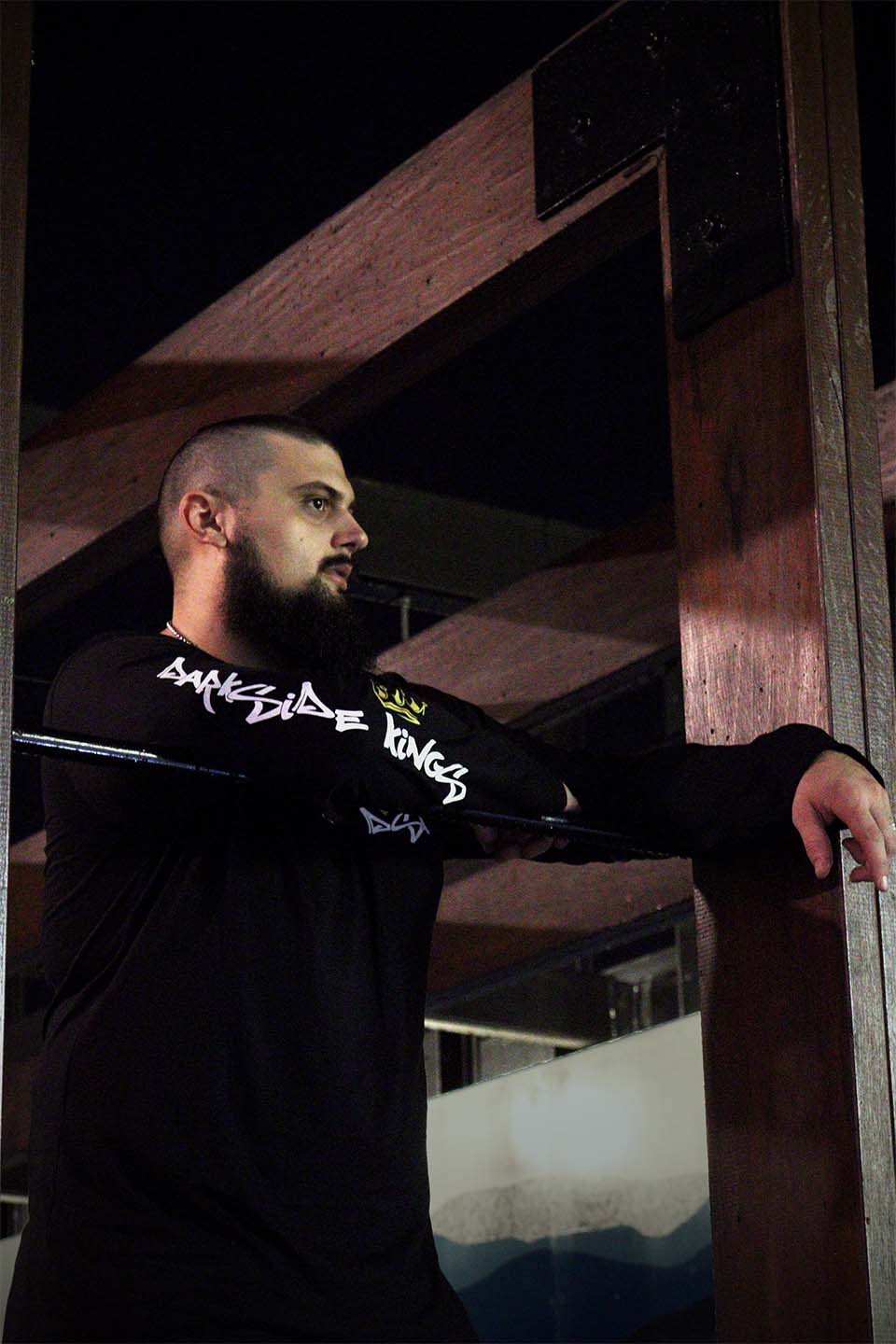 Male leaning over a rail wearing a black long sleeve shirt with a Darkside Kings logo printed down the sleeve