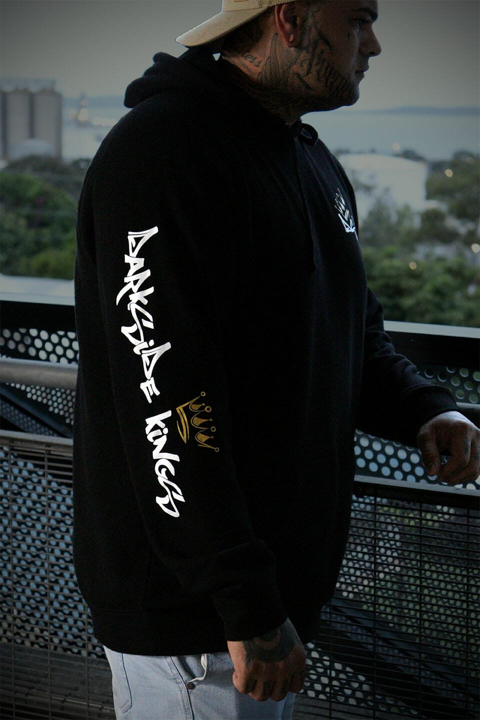 Male leaning over a rail wearing a black hoodie with a Darkside Kings logo printed down the sleeve