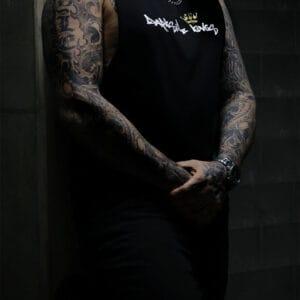 Male leaning against a concrete wall wearing a black Darkside Kings logo singlet