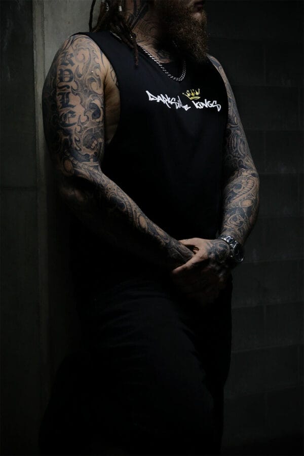 Male leaning against a concrete wall wearing a black Darkside Kings logo singlet
