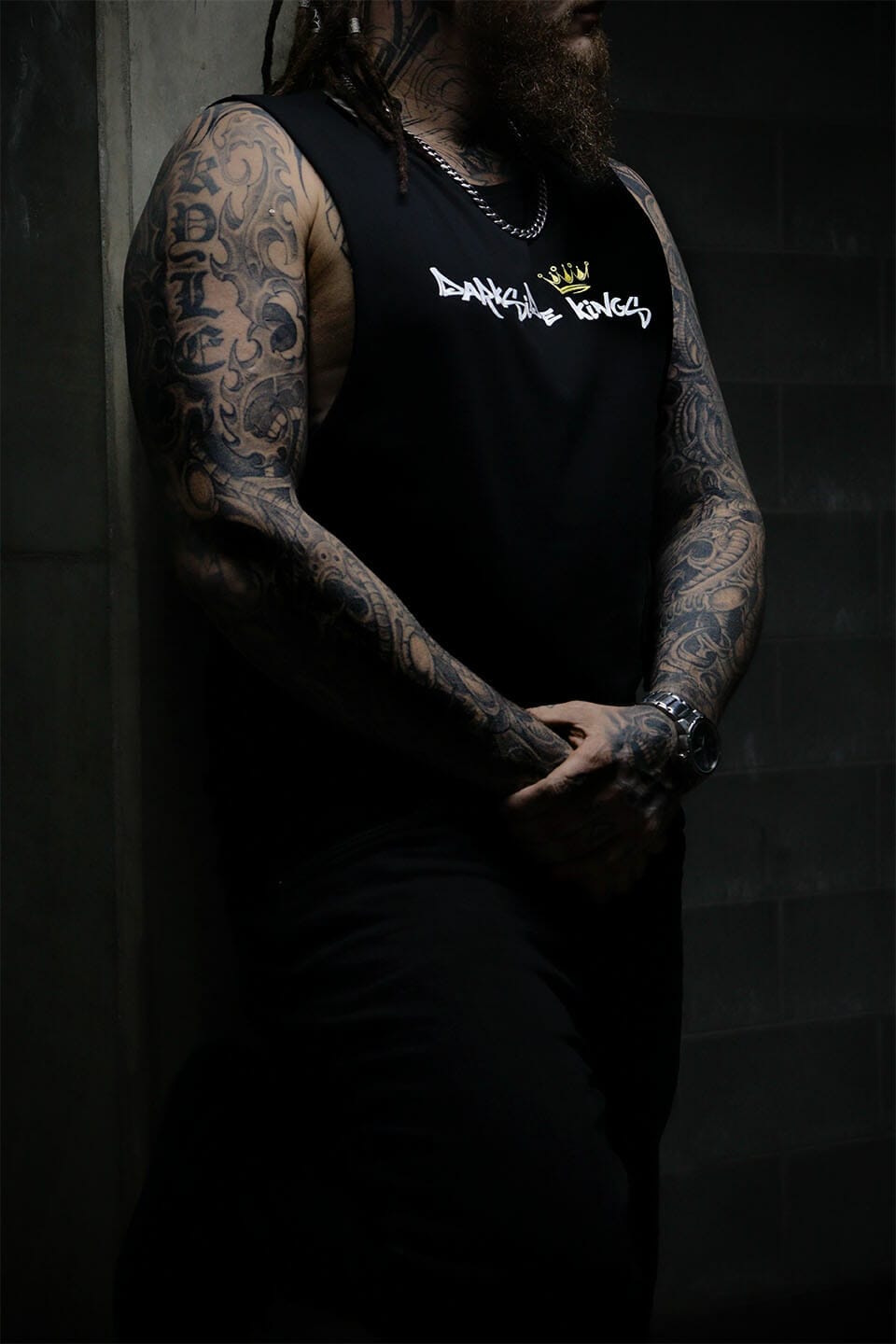 Male leaning against a concrete wall wearing a black Darkside Kings logo singlet