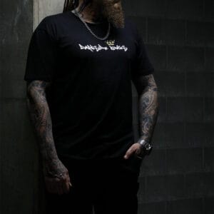 Male leaning against a concrete wall wearing a black Darkside Kings logo t-shirt