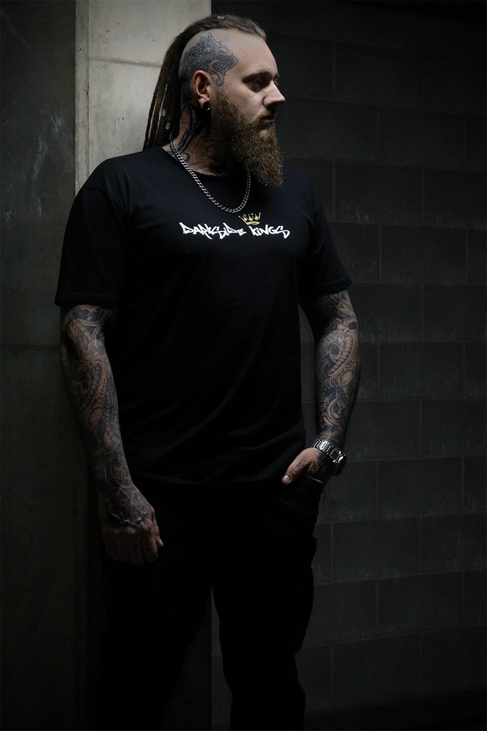 Male leaning against a concrete wall wearing a black Darkside Kings logo t-shirt