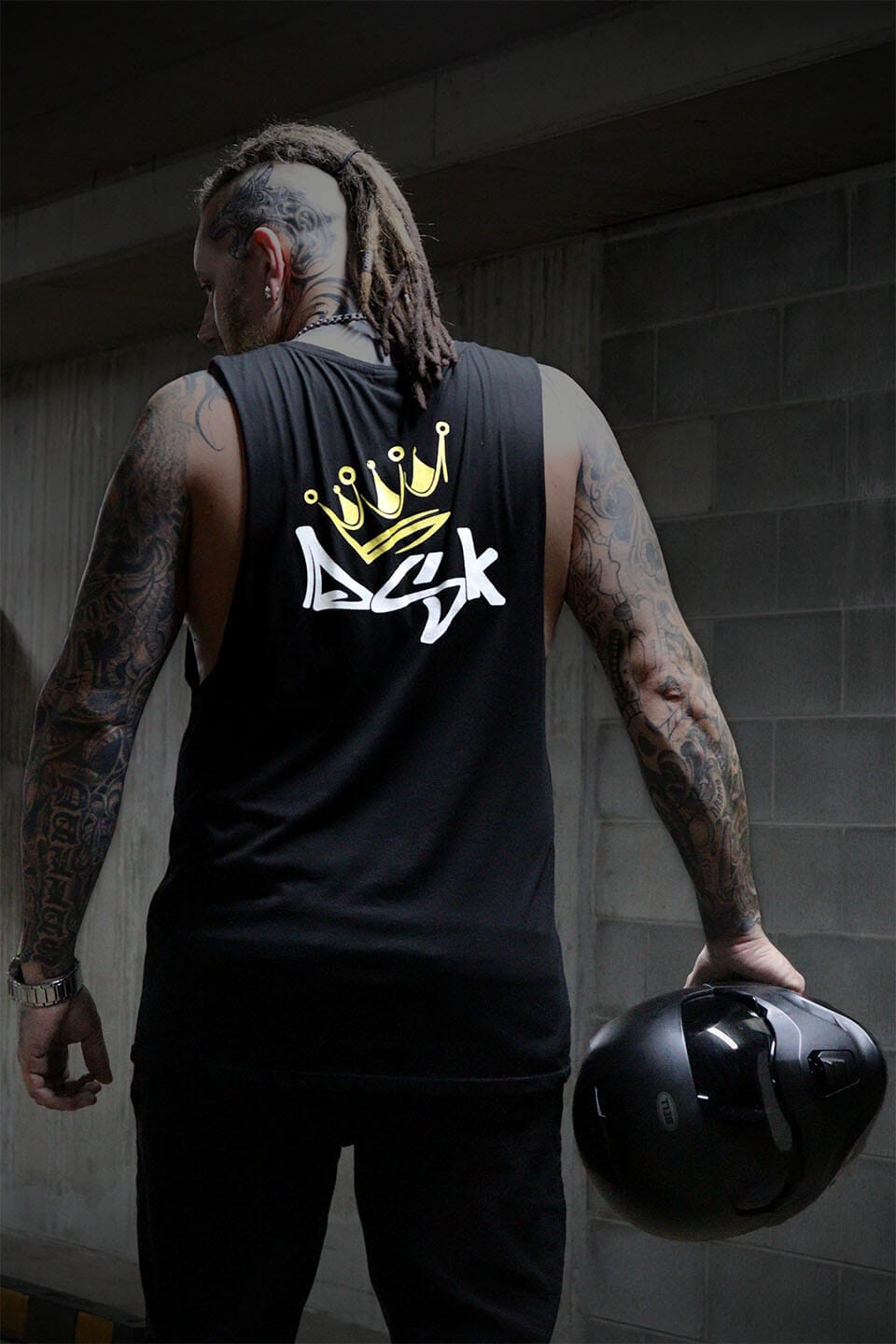 Male wearing a black DSK logo tank top singlet and holding a black motorcycle helmet