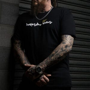Male leaning against a concrete wall wearing a black Darkside Kings logo t-shirt