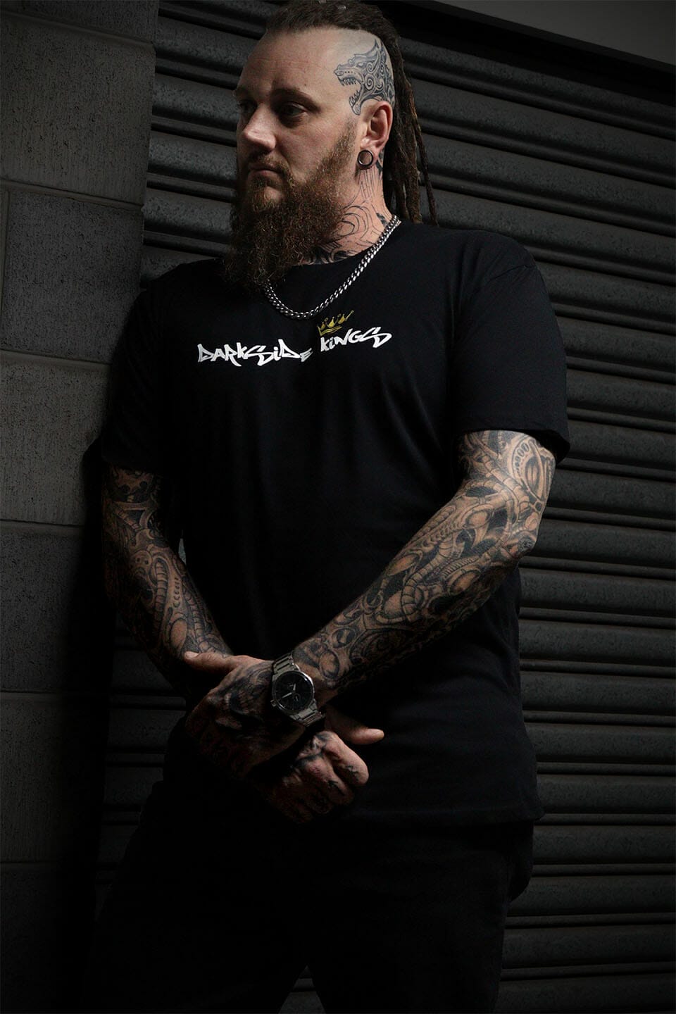 Male leaning against a concrete wall wearing a black Darkside Kings logo t-shirt